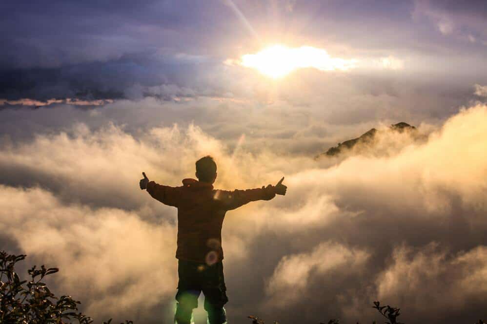 man celebrating on mountain surrounded by clouds